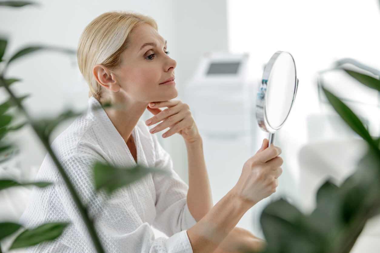 skin tightening woman looking into mirror with plants in the foreground the eye wearhouse